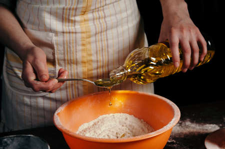 Female hand pour sunflower oil in a bowl with the flour. Preparation of the test. A drop of oil. Beautiful.の写真素材
