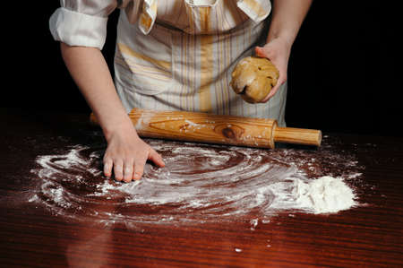 A woman in the kitchen is rolling a dough on a wooden table with a wooden rolling pin.の写真素材