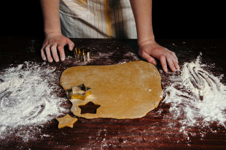 The girl in an apron cuts dough shaped cookies in the form of stars on a wooden table. Close-up.の写真素材