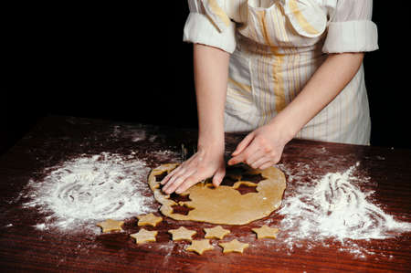 The girl in an apron cuts dough shaped cookies in the form of stars on a wooden table. Close-up.の写真素材