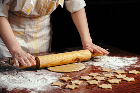 A woman in the kitchen is rolling a dough on a wooden table with a wooden rolling pin. She molds cookies in the form of asterisks.の写真素材