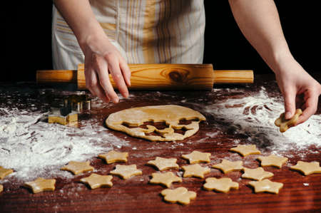 A woman in the kitchen is rolling a dough on a wooden table with a wooden rolling pin. She molds...