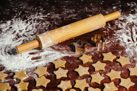 On the old wooden table lies a rolling pin with flour and raw dough in the form of asterisk. Christmas cookies.の写真素材