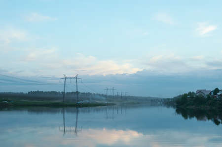 Evening misty landscape of the countryside. The river is in a fog. Wires of electric voltage.の写真素材