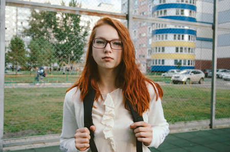 Portrait of a smiling red-haired girl with red glasses on the background of high-rise buildings.の写真素材