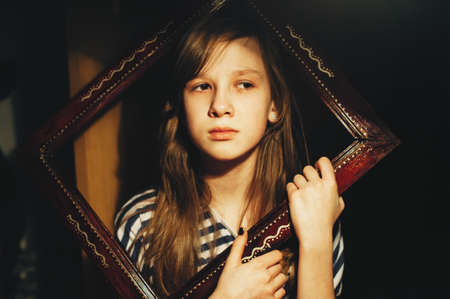 Portrait of a sad little girl looking out of a wooden frame. Child. Atmospheric photography. Conceptual.の写真素材