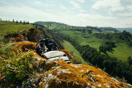 A backpack with photographic equipment rests on a rock with a view of the mountain landscape.の写真素材