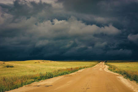 Dramatic dark storm clouds and dirt road to the horizon line.の写真素材