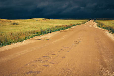 Dirt road to the horizon line under dramatic dark storm clouds.の写真素材