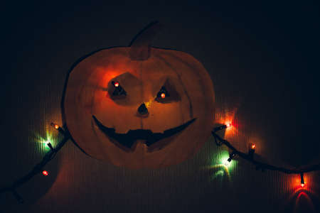 A paper pumpkin with a flashing garland in place of the eyes, hanging on the wall. A horrible template for Halloween.の写真素材