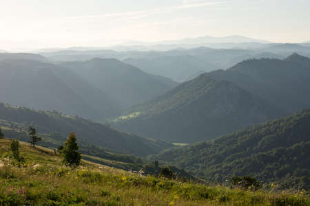 A mountainous misty landscape in the dawn rays of the sun. In the distance, one can see many layers...