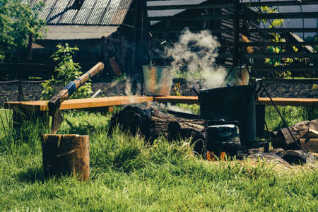 Russian country comfort.
The ax in the stump.
A kettle and a large saucepan at the stake.
A bucket on the bench.
Everywhere grass.
Against the backdrop of a village house.の写真素材
