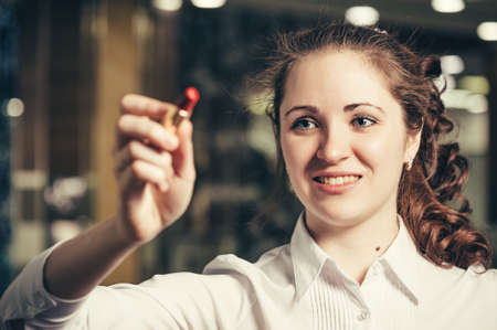 Young girl writes (draws) bright red lipstick on glass. Business woman uses a lipstick instead of a...