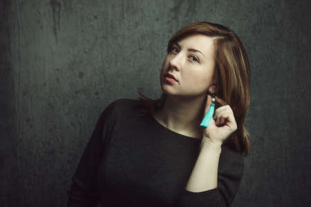 Vintage portrait of beautiful stylish girl with turquoise earrings on gray studio background.の写真素材