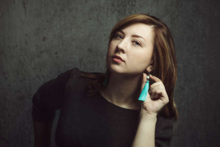 Vintage portrait of beautiful stylish girl with turquoise earrings on gray studio background.の写真素材