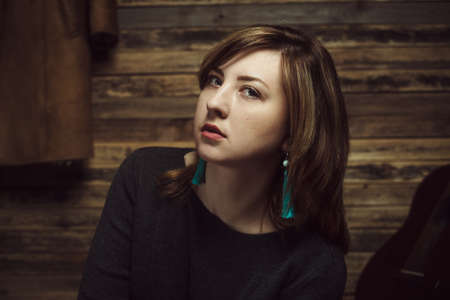Vintage portrait of beautiful stylish girl with turquoise earrings in old wooden hut.の写真素材