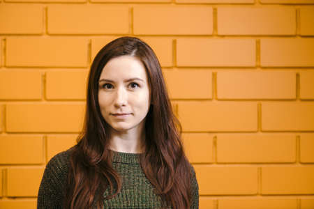 Beautiful red-haired girl wearing glasses and a green sweater is smiling against a yellow brick wall background.の写真素材