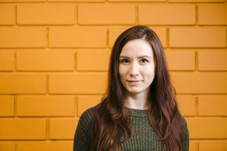 Beautiful red-haired girl wearing glasses and a green sweater is smiling against a yellow brick wall background.の写真素材