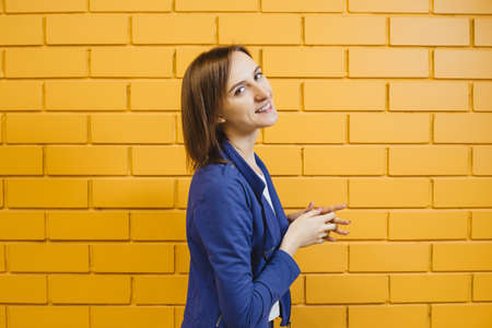 Beautiful cheerful modern blonde girl in a business pose against a yellow brick wall.の写真素材