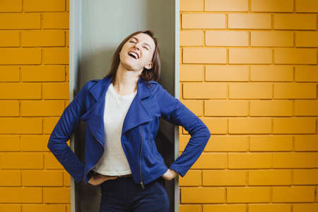 Beautiful cheerful modern crazy blonde girl squinting against yellow brick wall.の写真素材