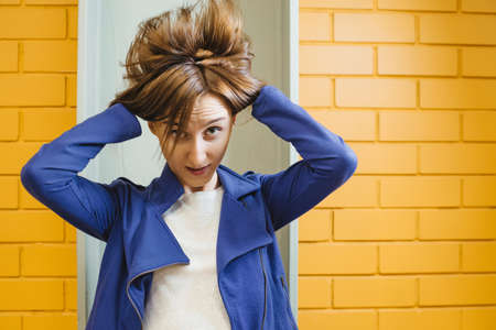 Beautiful cheerful modern crazy girl with flying blond hair against yellow brick wall. Sidelong glance.の写真素材