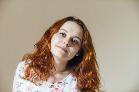 Portrait of beautiful cheerful redhead girl with curly hair over beige background. Hair dyed with henna. Professional hair care.の写真素材