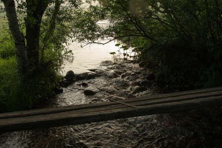 Wooden foot bridge across a small mountain stream flowing among bushes and trees. Reflex of sun...