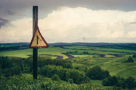 Dramatic green mountain landscape with road sign on background fields under cloudy sky.の写真素材