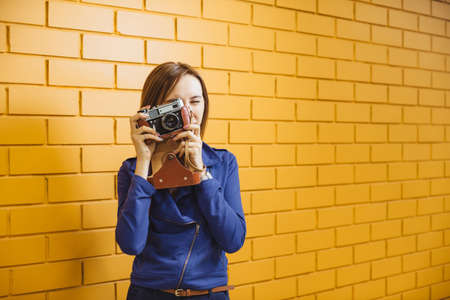 Beautiful crazy girl with retro metal film camera on background yellow brick wall.の写真素材