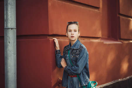 Curious little girl in jeans clothes stands near an old restored beautiful building.の写真素材