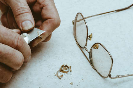 Table composition with glasses, pencil shavings and hands of elderly man who sharpens pencil with knife.の写真素材