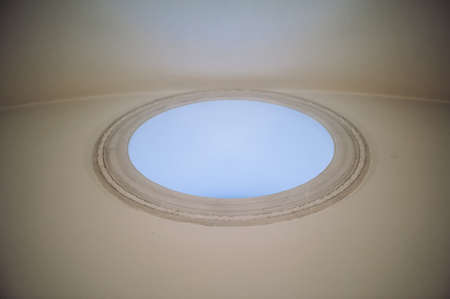 Circle window with blue sunlight on high wall under ceiling. Beautiful interior of temple in style...