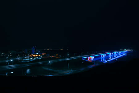 Night neon automotive bridge over river Ob in Barnaul city, Russia. Blue illumination of new Barnaul bridge. Cyan luminescence in night. Shot from height, 17 April 2018. View from upland park.のeditorial素材