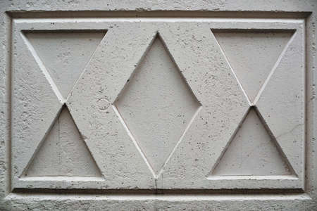 Old soviet concrete fencing with cracked surface with image in shape of rhombus and triangles close-up. Background image of grunge fence of unusual design. Urban white durable wall.の写真素材