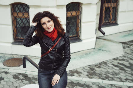 Rainy portrait of beautiful pensive girl with curly brown hair in black leather jacket, blue jeans,...