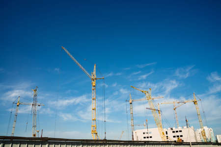 Big tower cranes above buildings under construction against blue sky. Background image of...