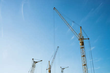 Big tower cranes against the blue sky. Background image of construction equipment close-up with copy...