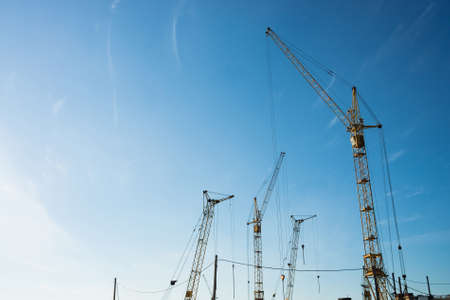 Big tower cranes against the blue sky. Background image of construction equipment close-up with copy space. Build of city.の写真素材