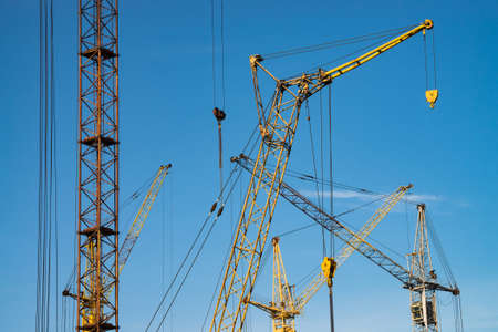 Big tower cranes against the blue sky. Background image of construction equipment close-up with copy...