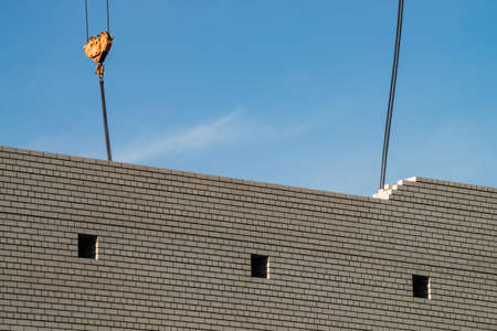 Hook of tower crane above unfinished building in construction site. Background image of white brick...