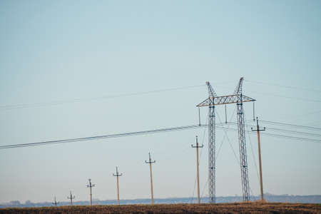 Atmospheric landscape with power lines in field under blue sky. Background image of electric tower with copy space. Wires of high voltage above ground. Electricity industry.の写真素材