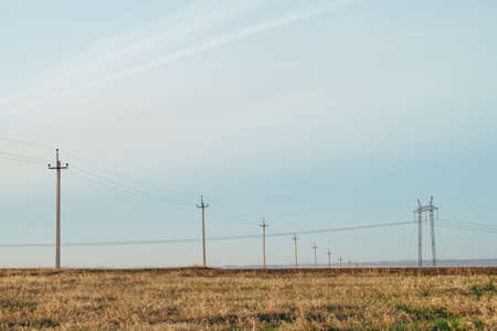 Atmospheric landscape with power lines in yellow field under blue sky. Background image of electric pillars with copy space. Wires of high voltage above ground. Electricity industry.の写真素材