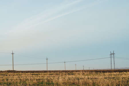Atmospheric landscape with power lines in yellow field under blue sky. Background image of electric pillars with copy space. Wires of high voltage above ground. Electricity industry.の写真素材