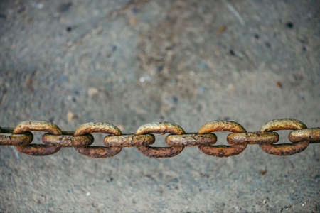 Old oxidized rusty chain hanging over asphalt close up with copy space. Conceptual background with thick links of strong chain. Artwork.の写真素材