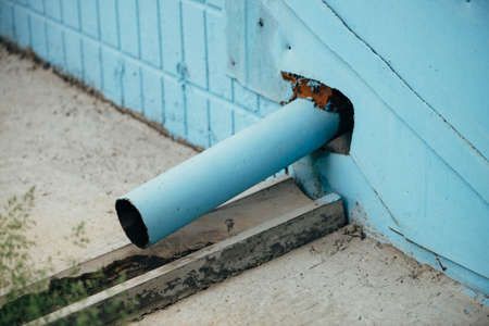 Blue drain pipe on cyan wall of building or home close up with copy space on tile. Green grass on foreground.の写真素材