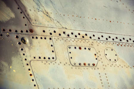Fragment of metal fuselage of old airplane with rusty bolts and scratches. Vintage background of surface of plane close up. Textured side of retro technology.の写真素材