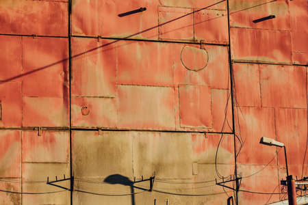 Red metallic wall of industrial building close up. Detailed background from large iron rusty panels with copy space. Shadow from lantern and wires on pink wall. Template with oxidised metal surface.の写真素材