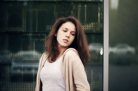 Fashionable carefree girl with mole on cheek in blouse of vanilla color enjoys waiting on background reflective window of store. Business woman looking dreamily into distance. Female pensive look.の写真素材