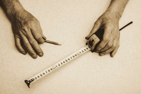 Hands of elderly working man with pencil and roulette close up in sepia tones. Monochrome background.の写真素材