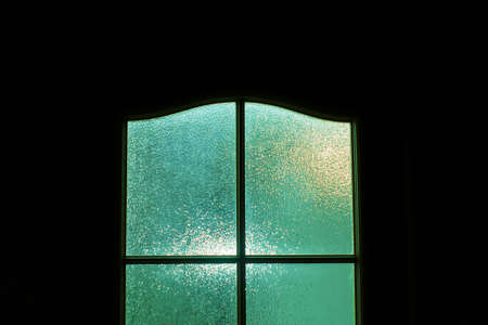 Dark silhouette of glass door in supernatural green light. Locked alone in room behind door on Halloween. Nightmare with aliens, monsters and ghosts. Evil in home. Inside haunted house. Alone in dark.の写真素材